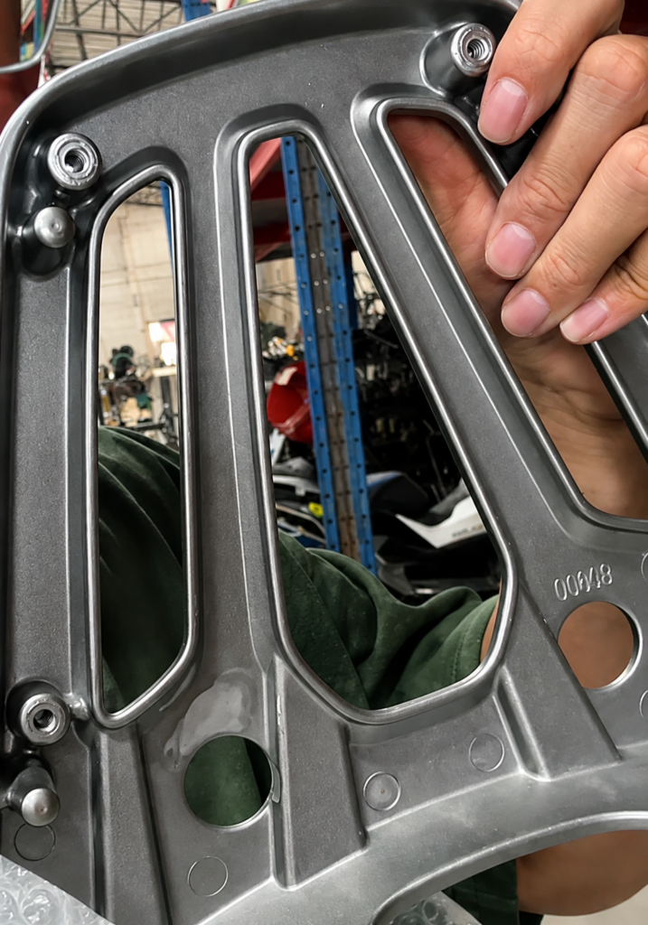 Hands holding a gray motorcycle rear rack near its mounting bracket and connection area