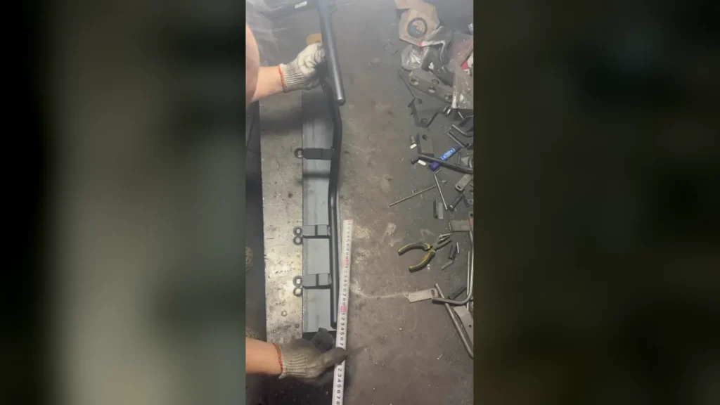 Worker measuring a PCX160 crash bar fixture with a ruler